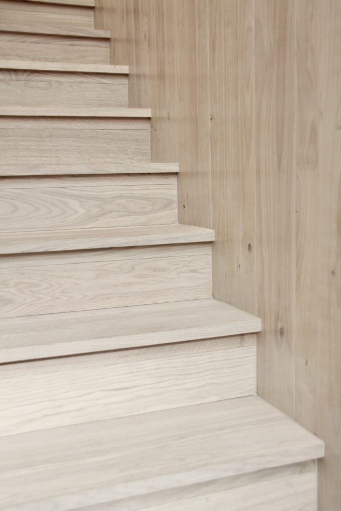 Whitewashed CLT wall meeting timber stair detail.